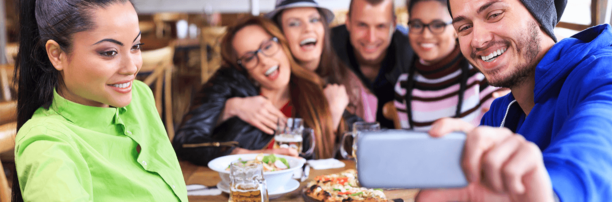 Group of friends taking selfies at a restaurant to post on Snapchat.