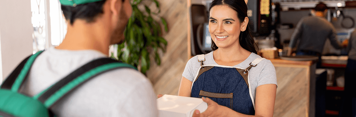 Restaurant server handing delivery person a to-go order.