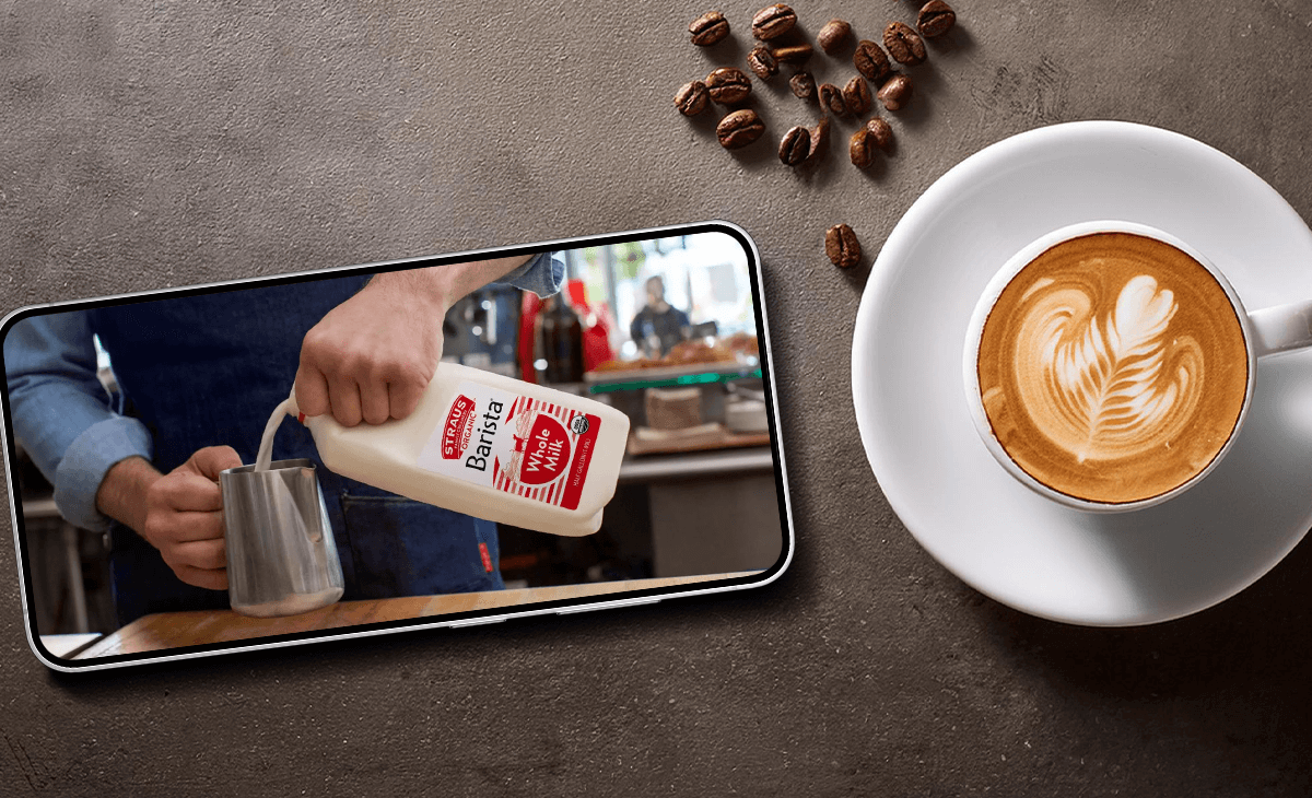 Straus Creamery Barista Milk video playing on a phone next to a cappuccino.
