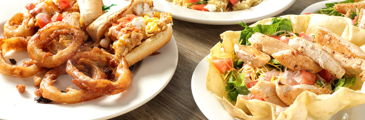 Chicken sandwiches and salads on white plates and bowls on a counter