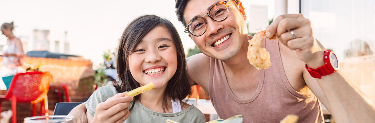 A young girl and her dad sitting at a table on a restaurant patio eating an early dinner.