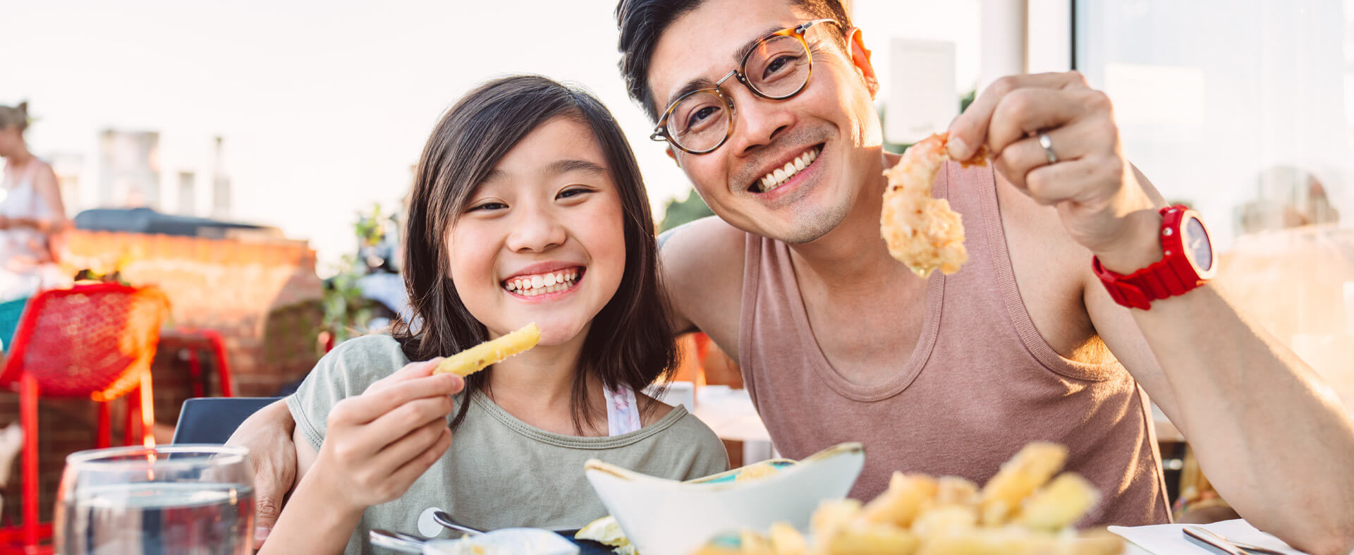Asian father and daughter sharing a meal at an outdoor restaurant.