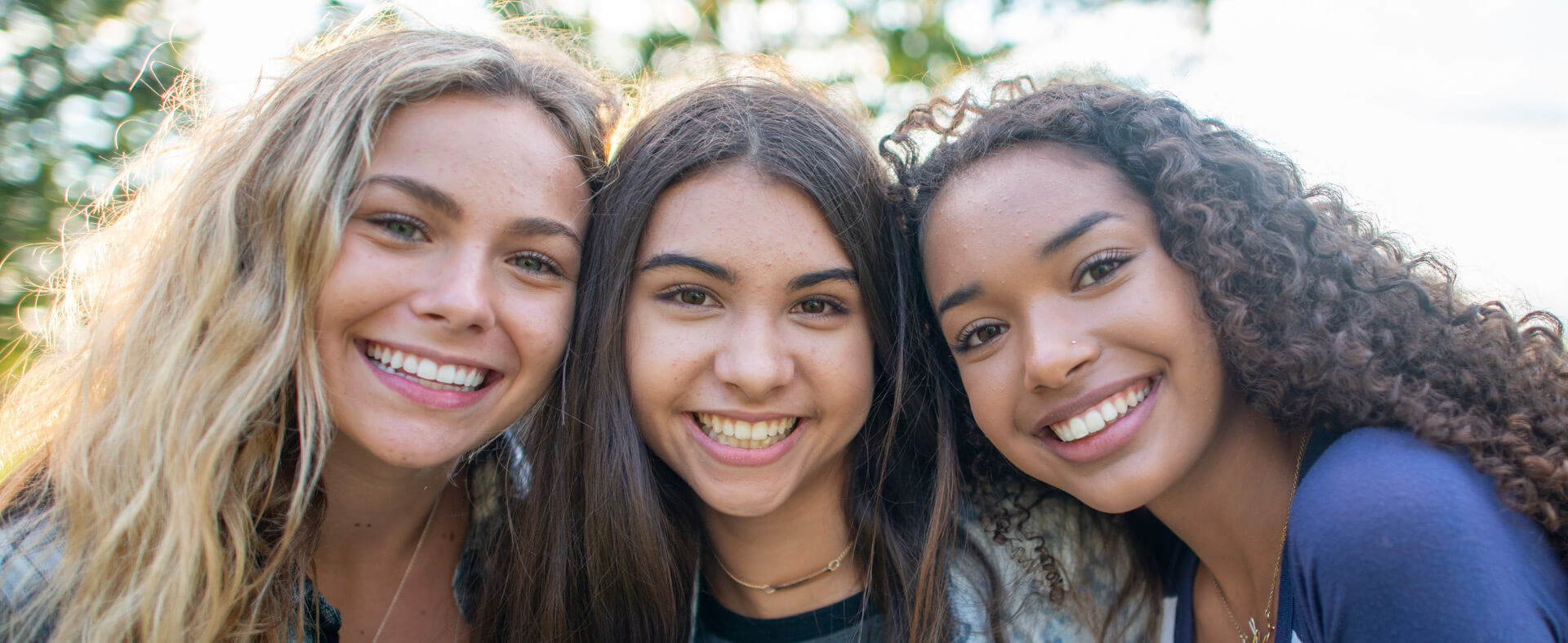 Three multi ethnicity teen girls posing for a picture outside.