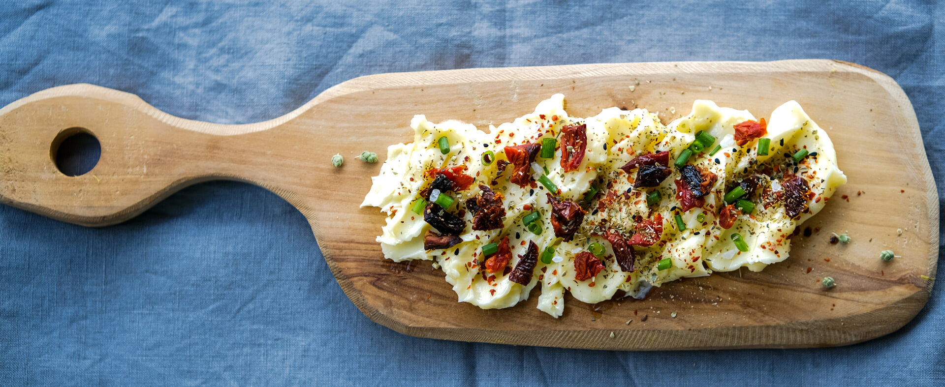 Creamy butter on a board topped with paprika, green onions and roasted tomatoes.
