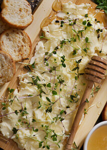 Butter board with sprouts and honey drizzle with toasted bread slices.