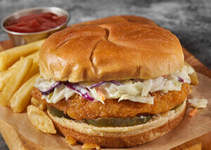 Hot Chicken Sandwich with sriracha slaw and pickles on a board with fries.
