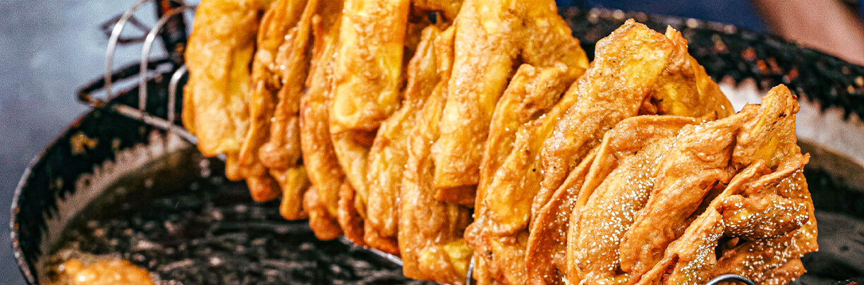 Fried dumplings snack on a long skewer drying over a pan of hot oil.