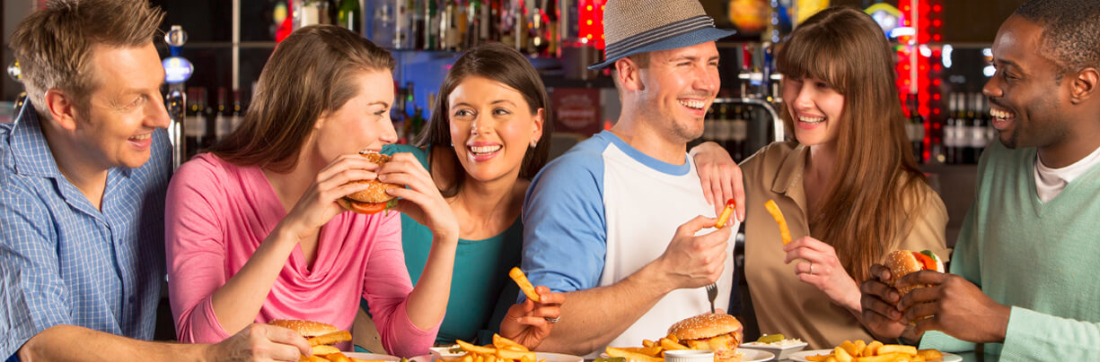 Three happy couple laugh and enjoy a meal of burgers and fries at a bar.