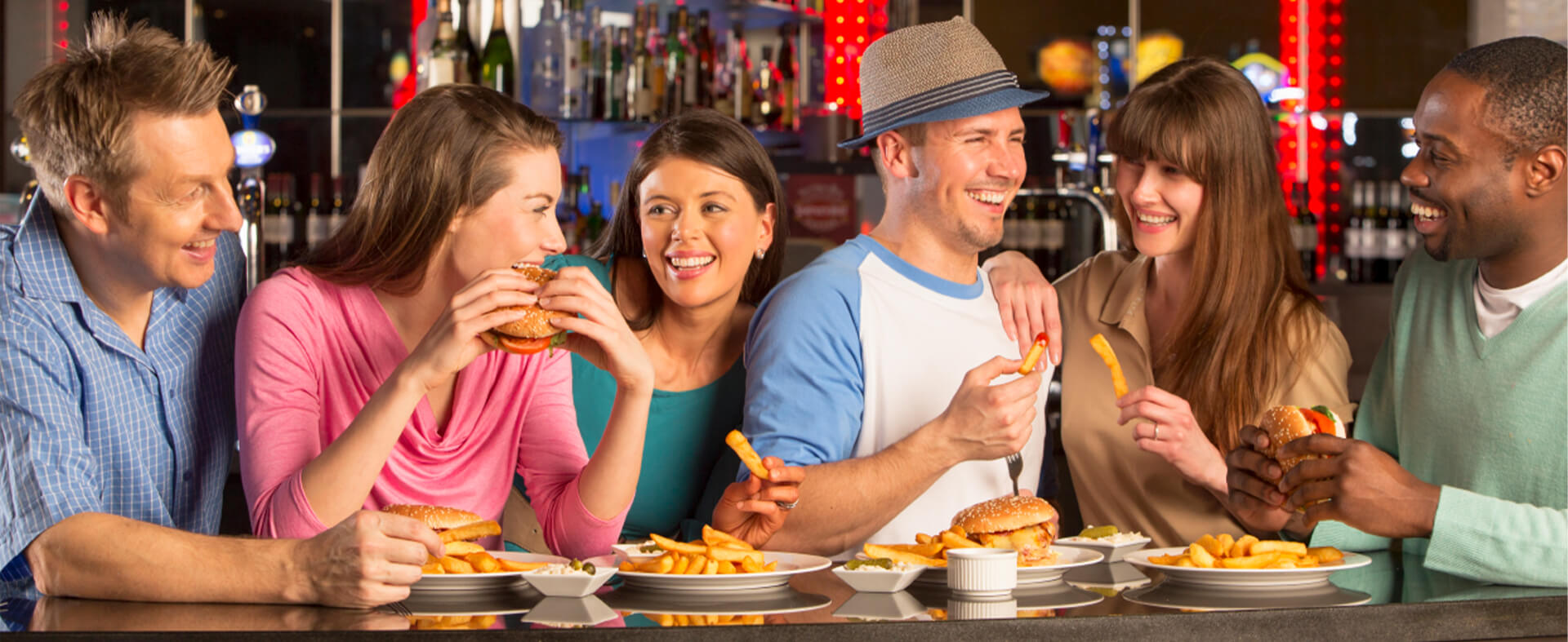 Six men and women friend enjoy a good time at a bar eating burgers and fries.
