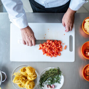 Overhead shot of a chef demonstrating chopping red peppers on a white cutting board.