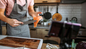 Chef blogger using a knife to show how to cut a salmon fillet over a cutting board.