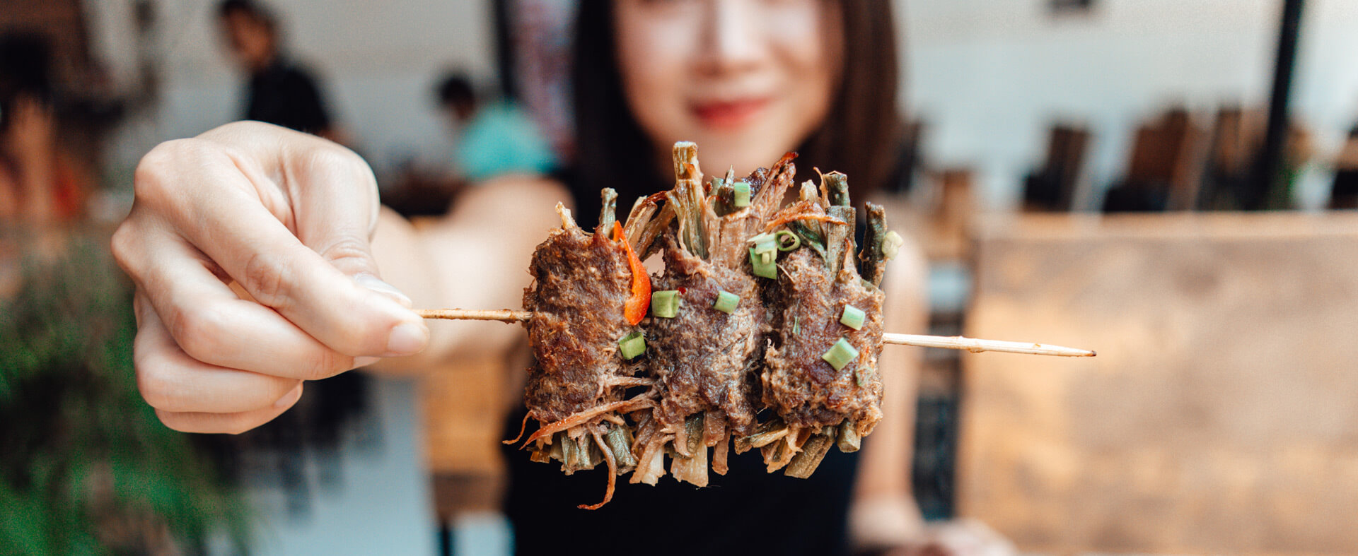 Close-up image of a young Asian female holding a beef skewer of Thai food in a Thai restaurant.