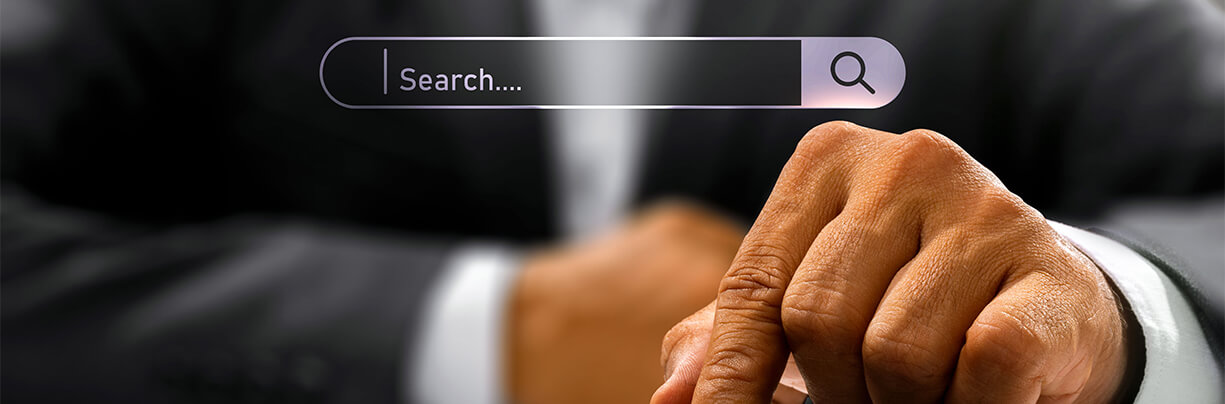 Search bar with a left hand of a male underneath that is pointing to a button on an iPad that is lying flat.