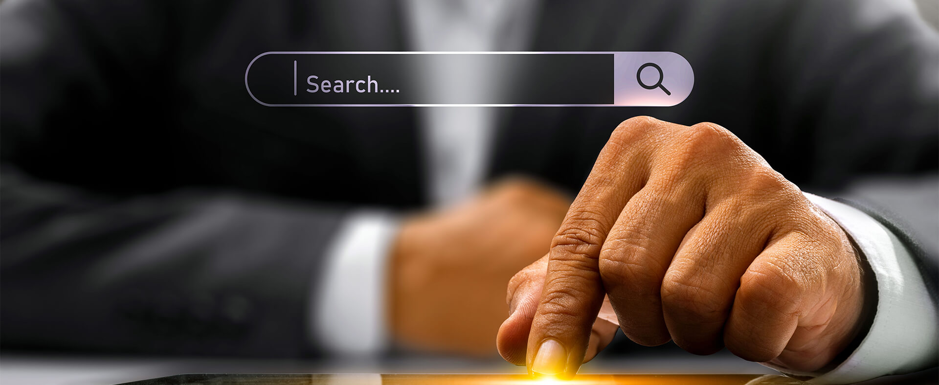 Male's left hand pressing a button on an iPad with a search bar hovering above hand.