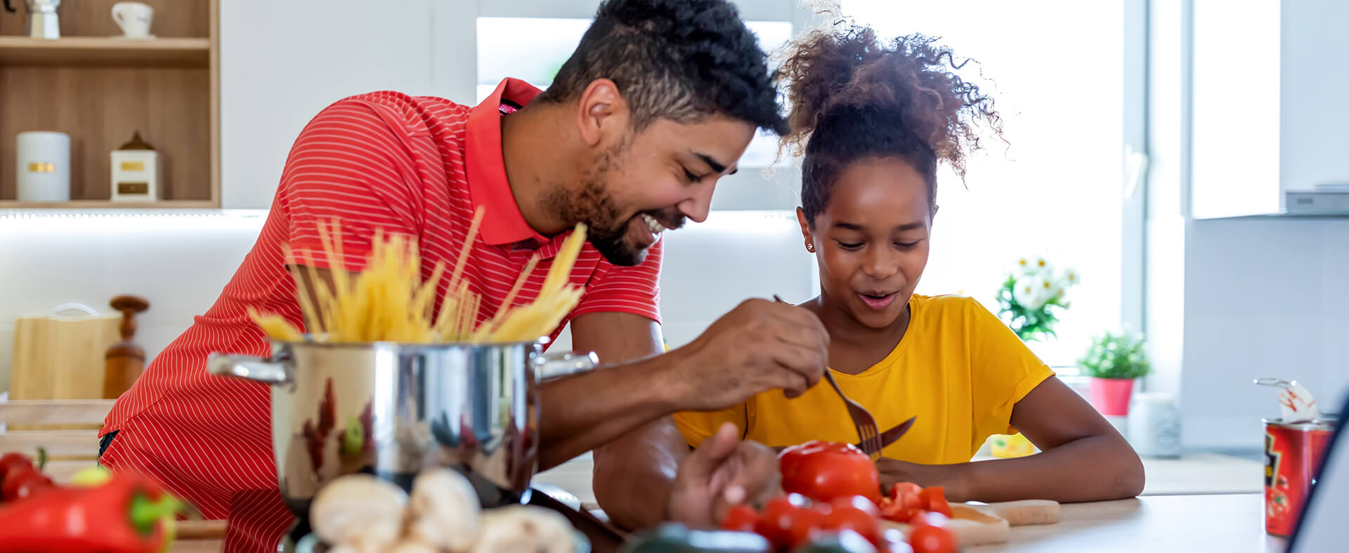 Black father and daughter making a healthy meal together in their kitchen.