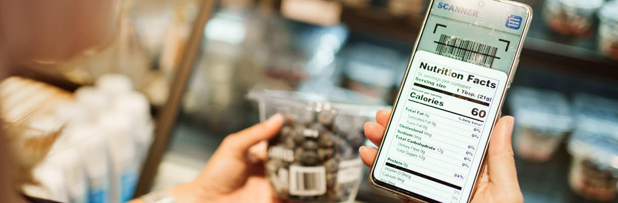 Female holding an iPhone in one hand and a package of chocolate-covered nuts in another while scanning the barcode for nutritional facts.