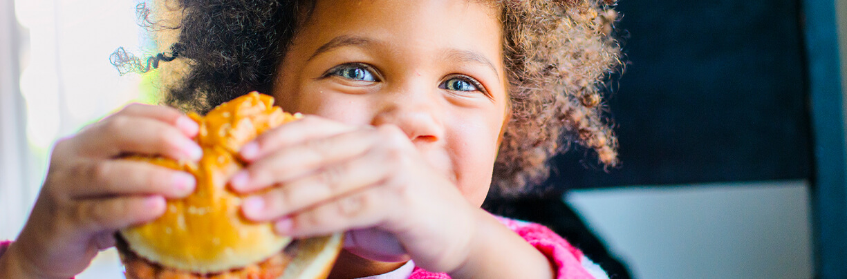 Close-up of a cute little boy holding a chicken sandwich with a bite out of it.