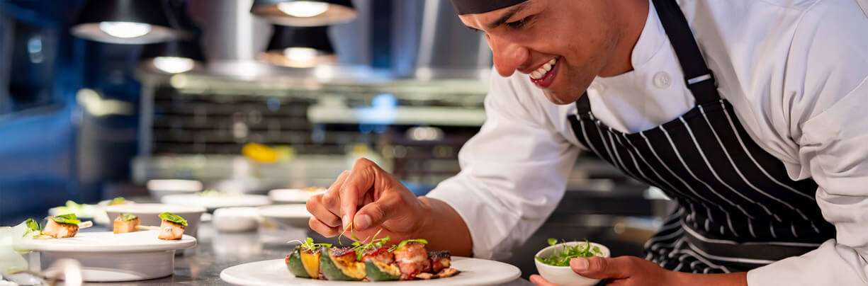 Young African American chef adding a greens garnish to a fine dining plated dish.