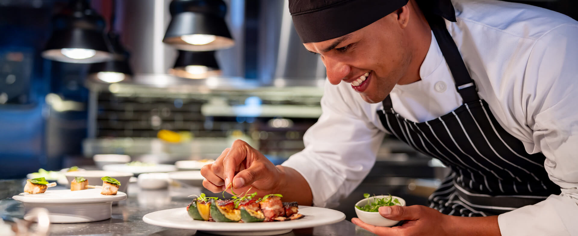 Young African American chef in a fine dining restaurant happily topping a dish with a greens garnish.
