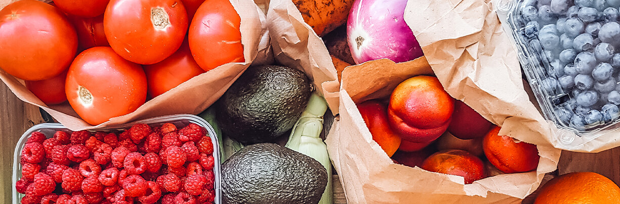 From tomatoes and raspberries to avocados and peaches, a group of fresh fruits on display in paper bags and plastic containers.