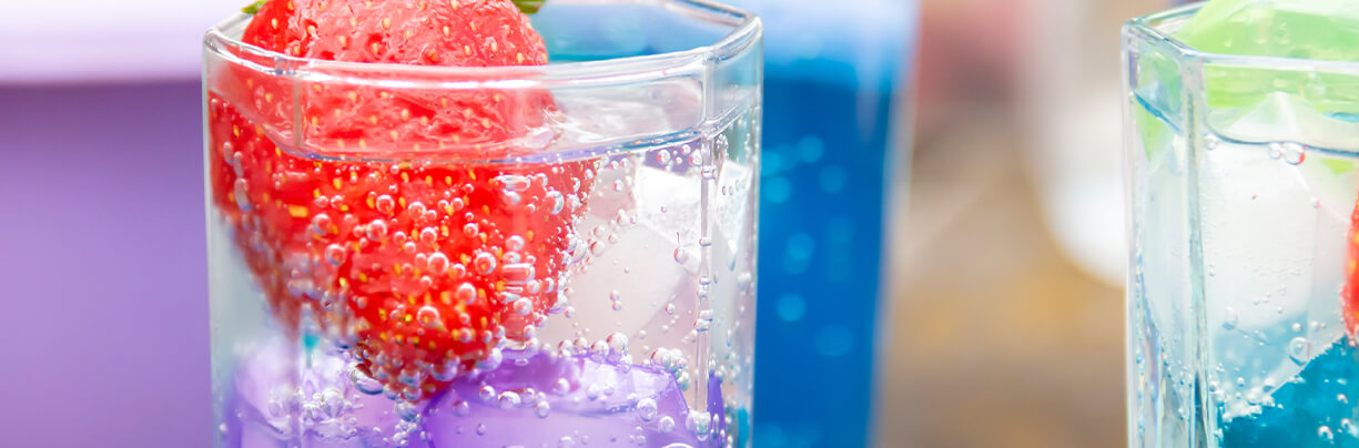 Close-up grouping of dirty soda drinks with fresh strawberry garnishes and blue-flavored syrup.