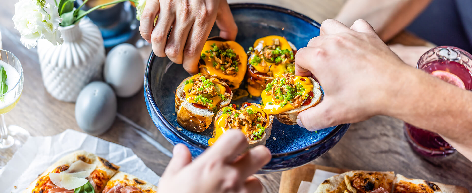 Group of hands each pulling a sample of an appetizer of a baguette with meat and cheese.