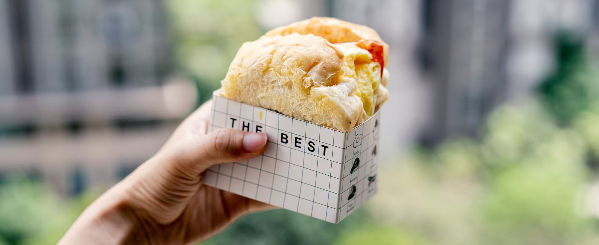 Handheld breakfast sandwich in a cardboard container being held by a hand.