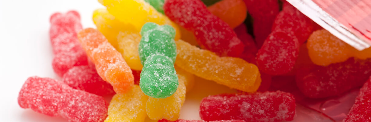 A close-up of an opened bag of sour gummy bears spilled out, showing the various colors and flavors.