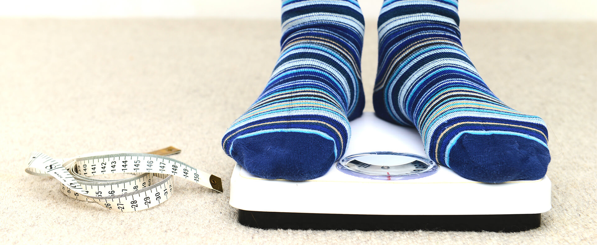 Close-up image of male feet in socks standing on a scale with a measuring tape on the side.
