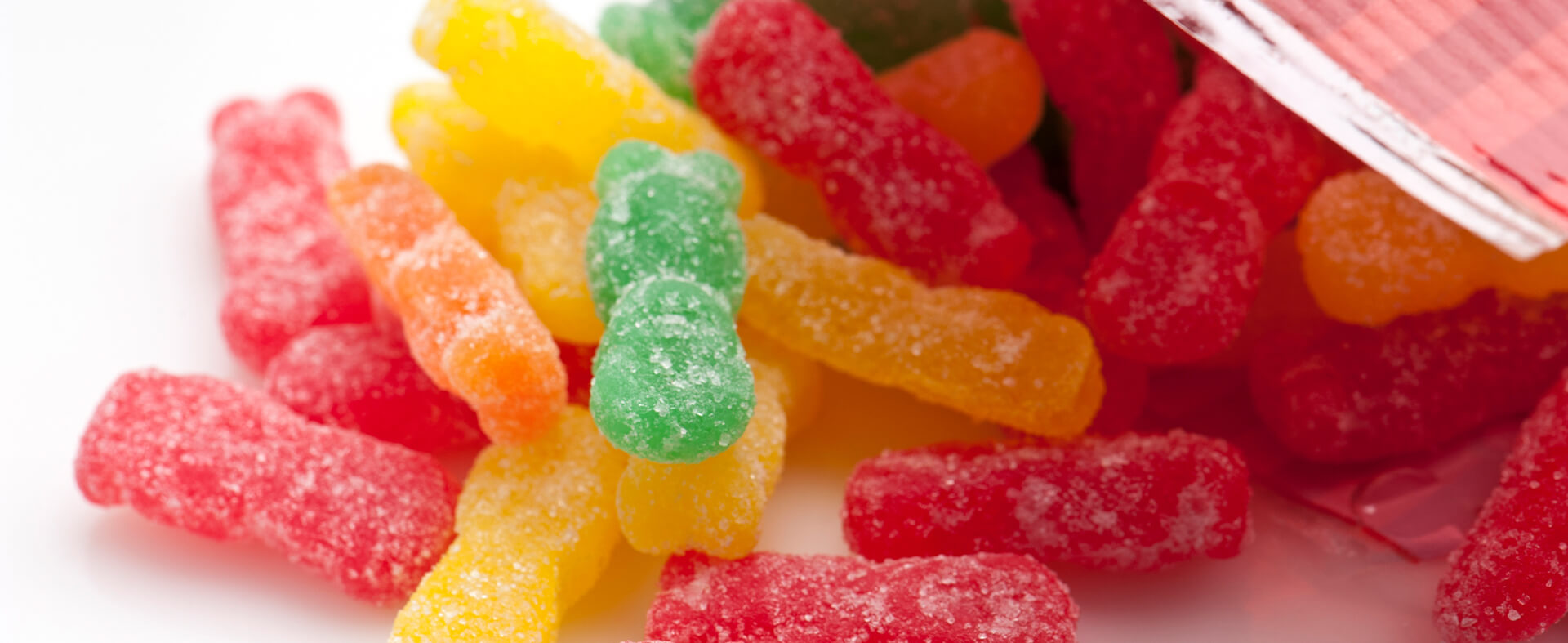 A close-up of gummy sugar candy bears in various flavors spilled out of a bag.