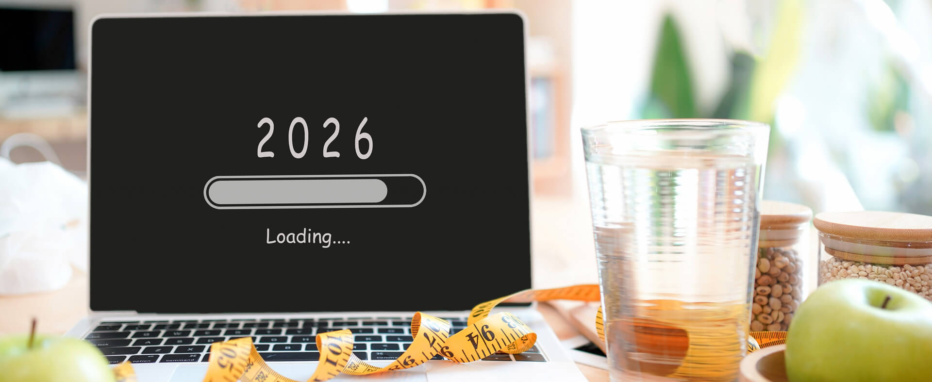 Laptop showing the year 2026 with a loading screen in black surrounded by a measuring tape, water and fruit.