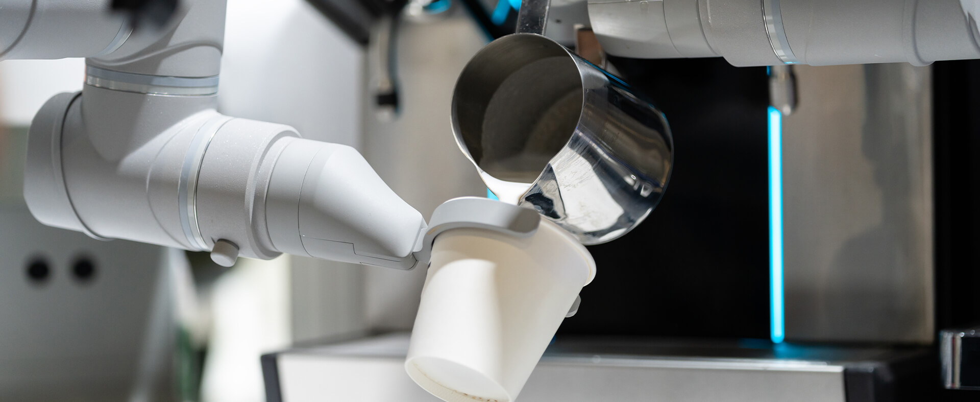 A close-up shows a robotic arm adding milk to a coffee drink. This happens in a quick-service restaurant.