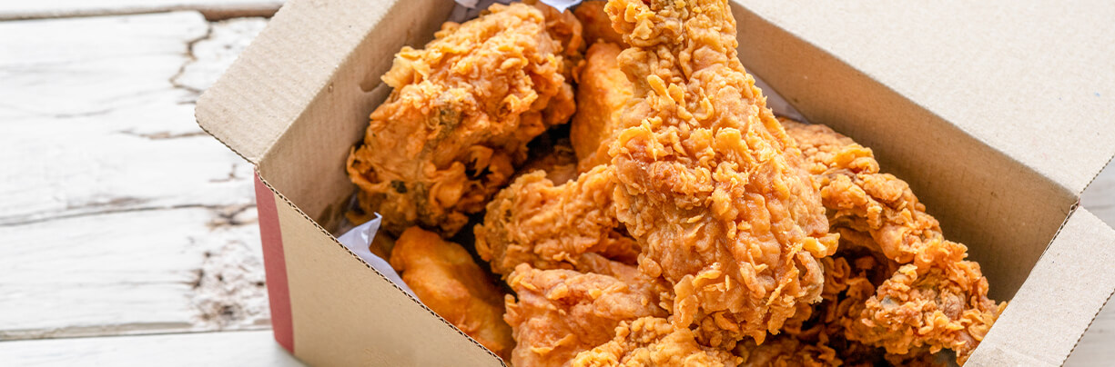 Three-quarter angle of a close-up box with fried chicken inside sitting on top of a white countertop.