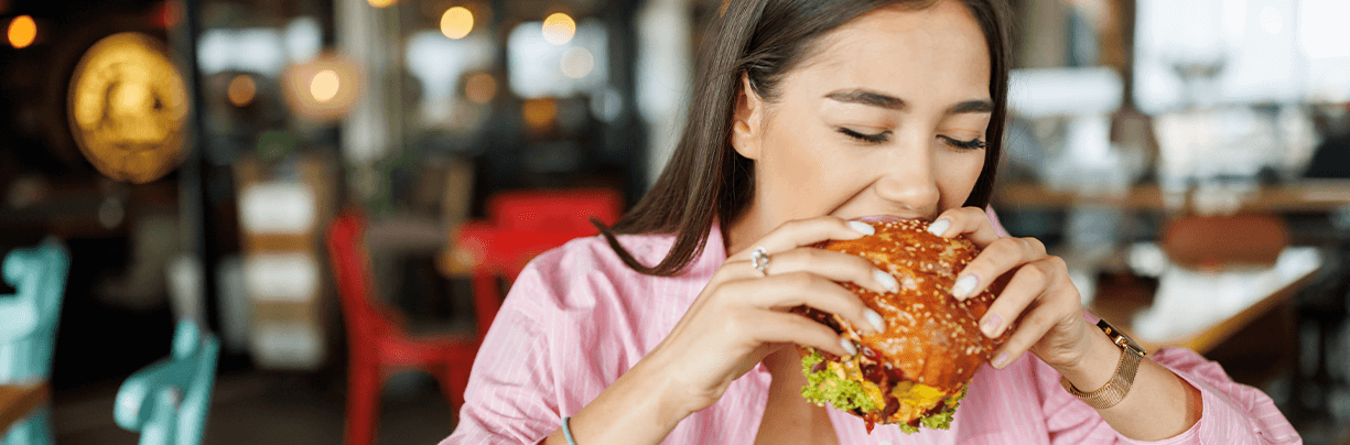 Female Gen Z taking a bite out of a burger in a casual dining restaurant.