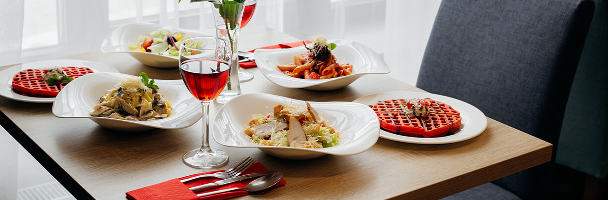 Valentine's Day restaurant dinner table with various pastas, salad, waffles and red wine.