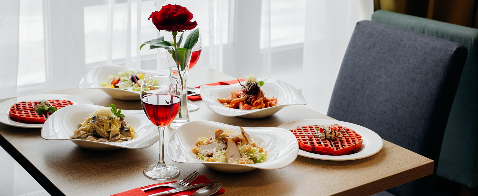 A romantic Valentine's Day dinner showing a restaurant table with pasta, salad, waffles and red wine.