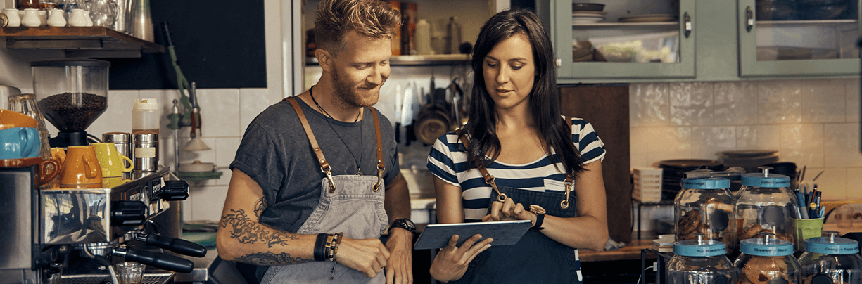 Gen Z male and female restaurant staff in a coffee shop reviewing food inventory on a tablet.