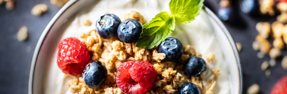 Close-up, top-down image of a bowl of Greek yogurt with oats, raspberries, and blueberries.