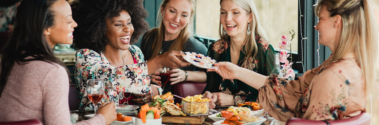 Five mixed-race females are enjoying dinner together at a restaurant.