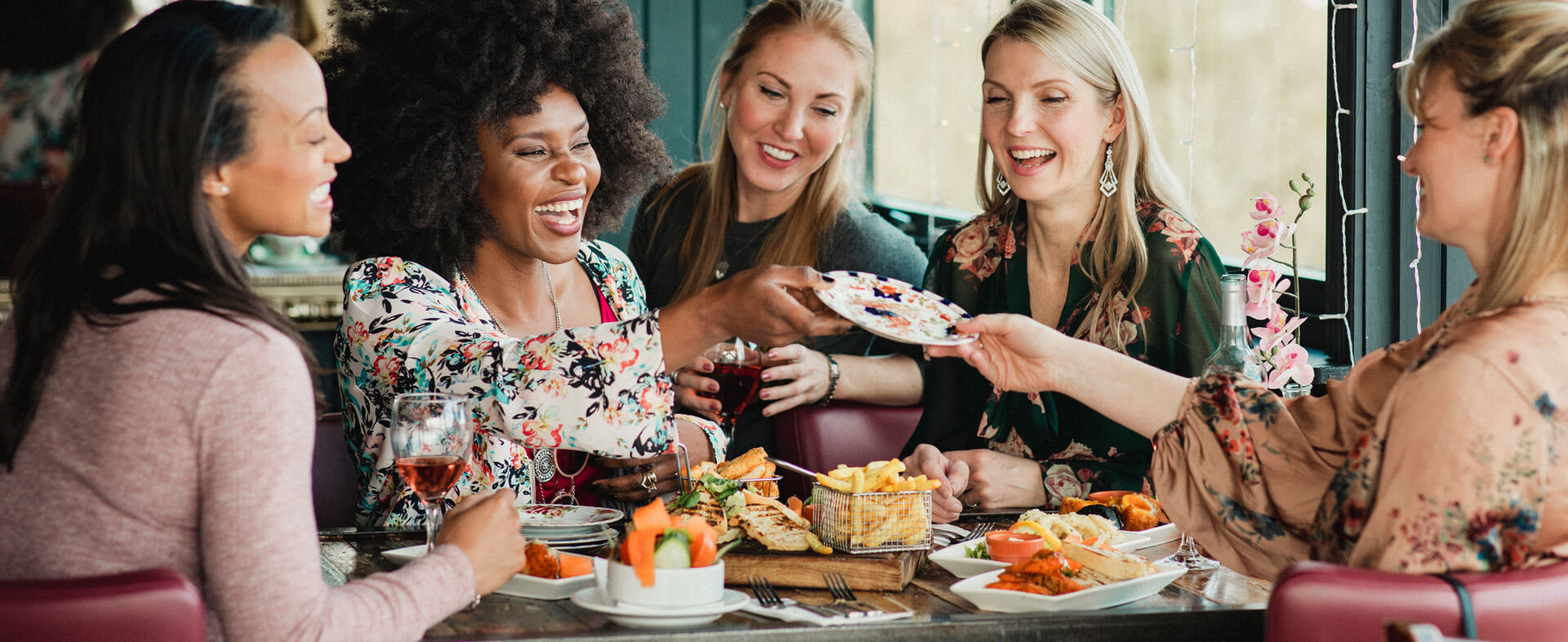 Female friends are laughing, passing appetizers across the table and eating dinner together at a restaurant.