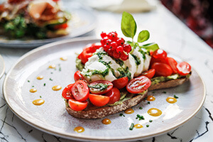 Close-up of a beautifully styled, plated avocado toast with cherry tomatoes, fresh mozzarella, and pesto.