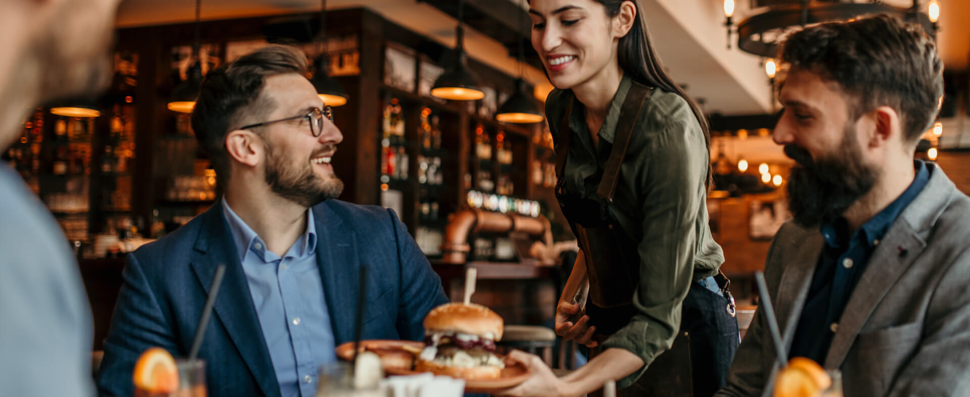 Happy female waitress serving a table of happy men burgers and drinks.